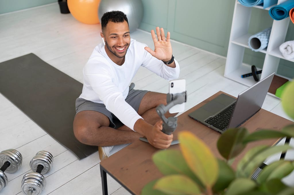 A man working out at home while greeting his online fitness trainer during a live video session.