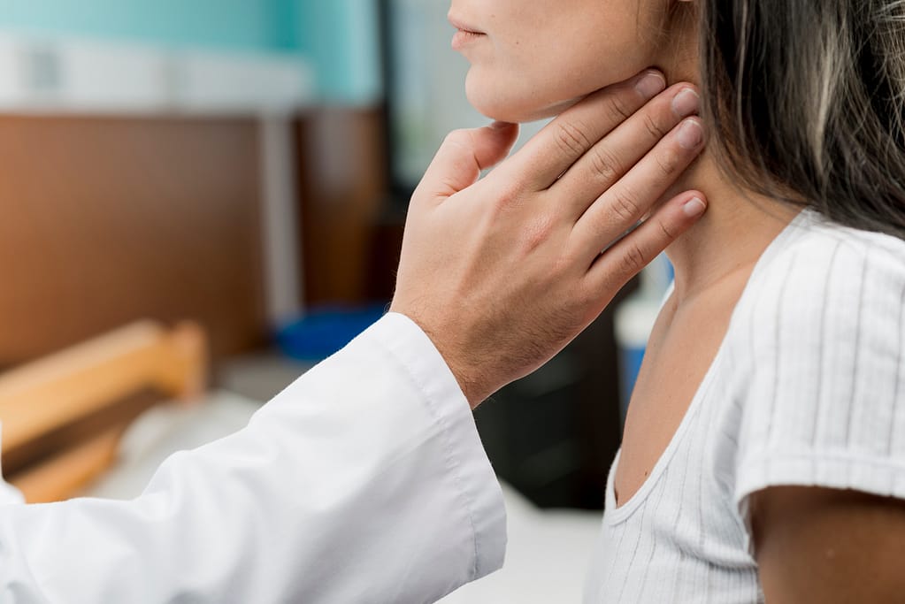 Doctor checking woman's thyroid for possible hyperthyroidism and weight issues.
