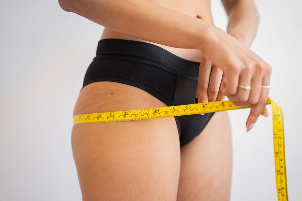 Woman measuring thigh with tape to track inches lost during weight loss.