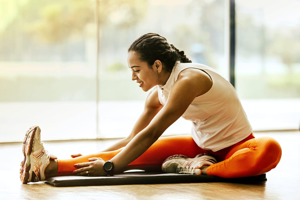 A woman stretches on a mat indoors, highlighting the difference between a Pilates mat and a yoga mat for various exercises.