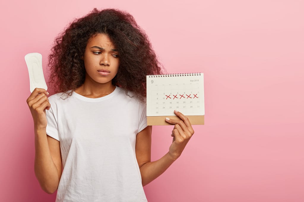 Woman holding a calendar and pad, confused about not losing weight but losing inches during her period.