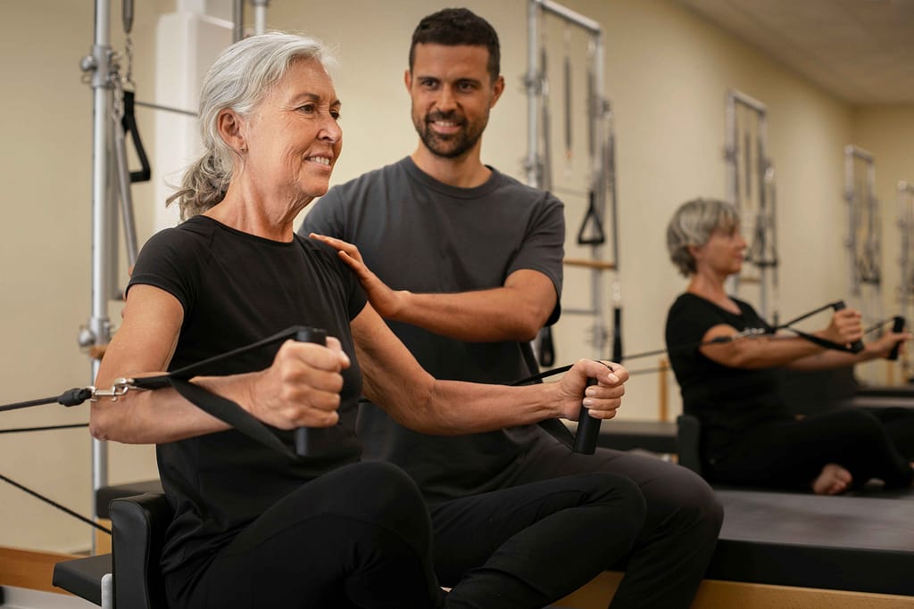 Senior women working with male personal trainers for seniors, using a Pilates ring to improve balance and strength.
