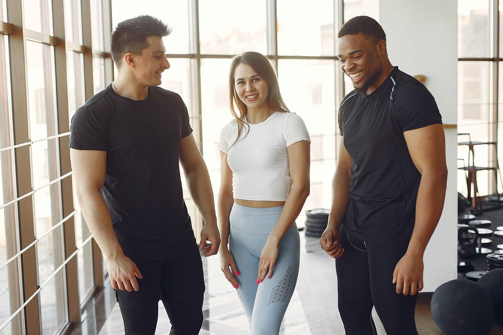 Personal trainers happy with a smiling client in a sunlit gym.