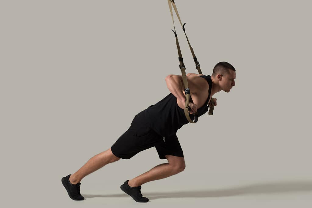 side-view-image-male-adult-gym_14_11zon A man performing a bodyweight chest fly using suspension straps as part of chest isolation exercises to strengthen and tone the pectoral muscles.