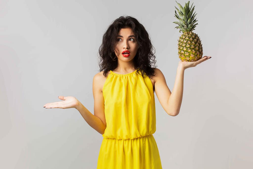 Surprised woman holding a pineapple, exploring the benefits of Pineapple for Weight Loss.