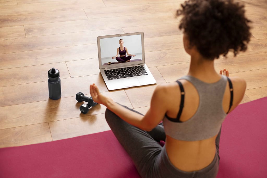 Affordable Personal Trainers Woman doing an online training session at home with a virtual trainer on her laptop screen.
