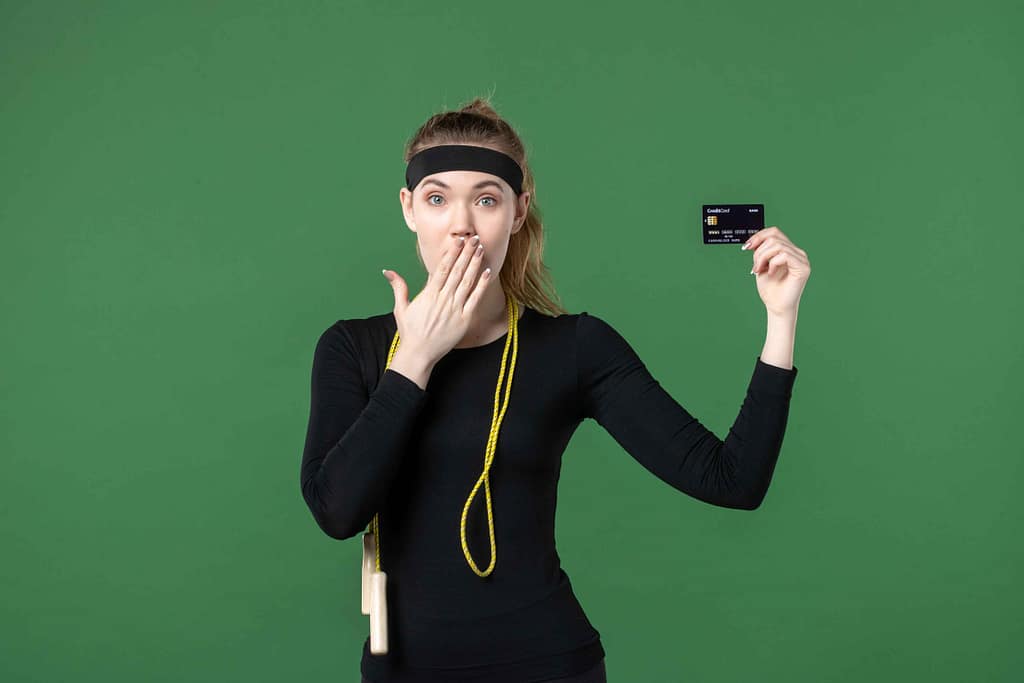 Average Cost of a Personal Trainer in Toronto Surprised young woman in workout clothes holding a credit card—fitness cost concept.