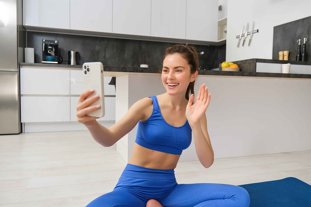 A woman waving at her trainer while beginning an online personal training session at home.