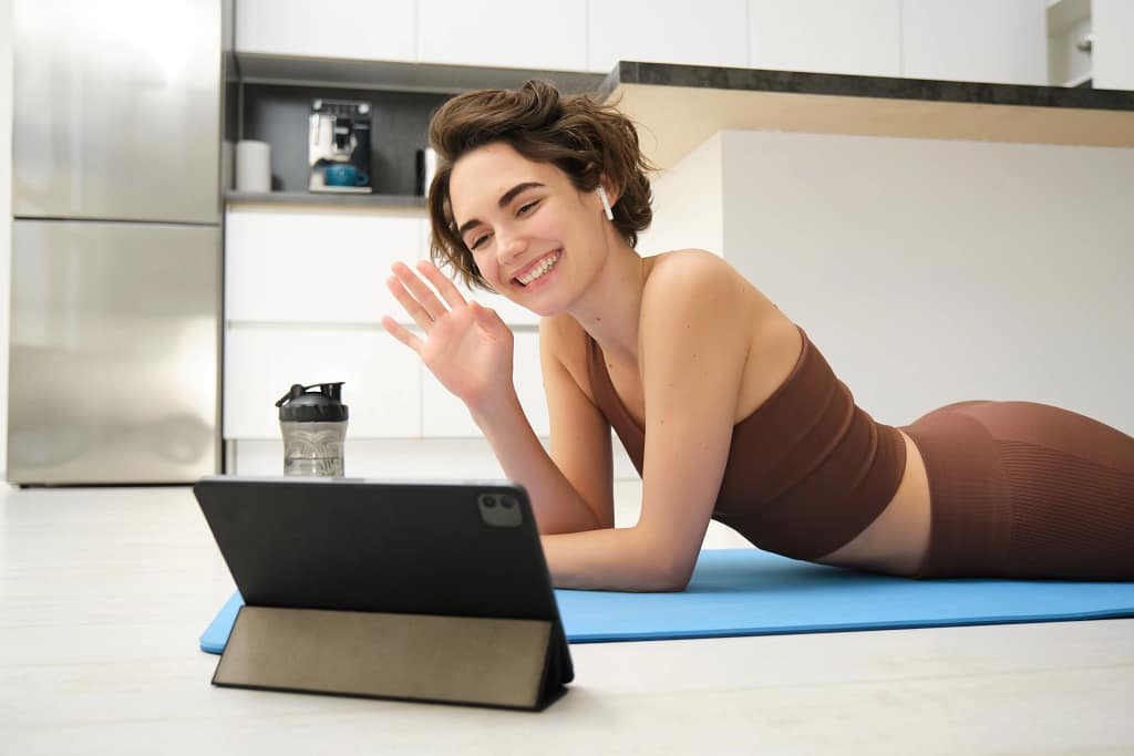 woman fitness A smiling woman in sportswear is training with her online personal trainer on a tablet at home.