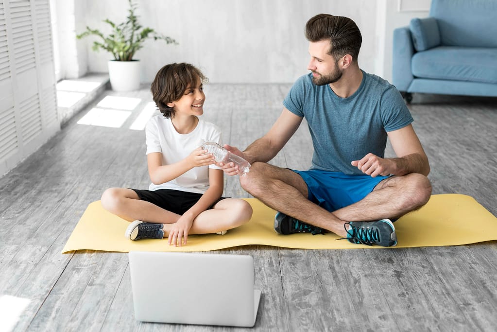 A teen exercising with his dad at home while following guidance from Online Personal Trainers for Teenagers on a laptop.