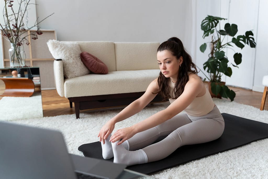 A woman stretching on a yoga mat at home while following her online yoga instructor on her laptop.