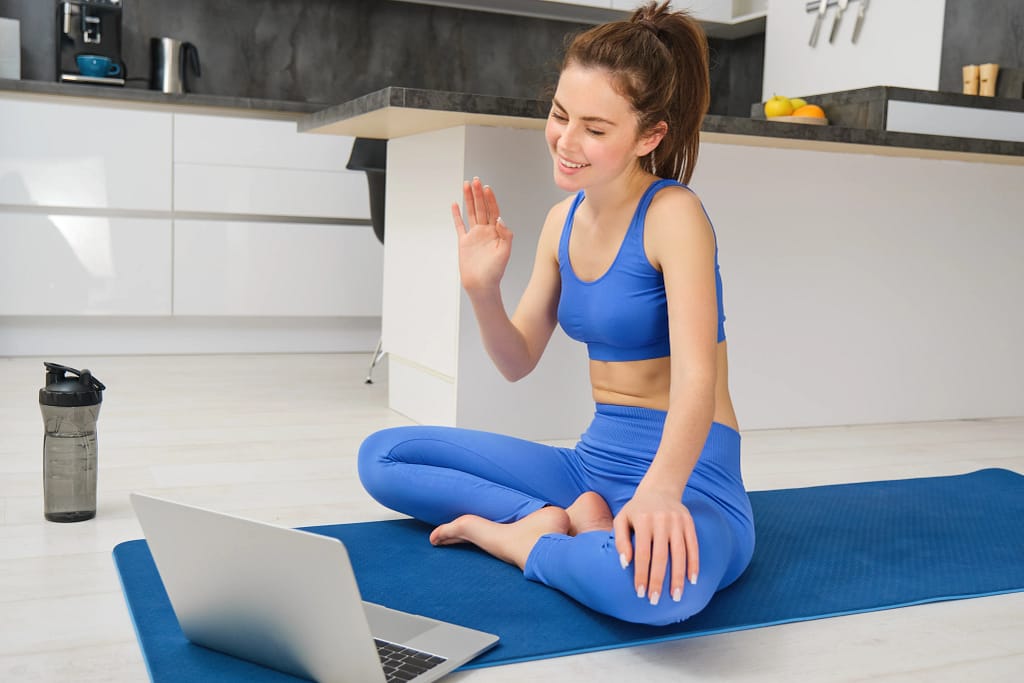 A young woman joining an online yoga for beginners session on her laptop.