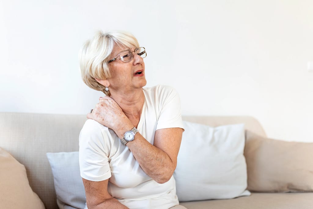 A senior woman sitting at home with neck pain, showing why guidance from an online fitness trainer for seniors matters.