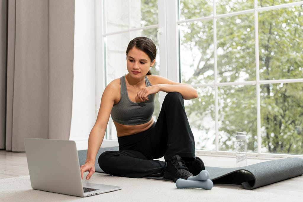 Online Corrective Exercise Specialists A woman exercising at home while following guidance from online corrective exercise specialists on a laptop.