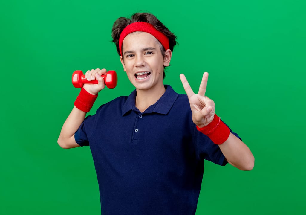 A cheerful teenage boy holding a red dumbbell and posing after an online workout with his fitness trainer for teens.