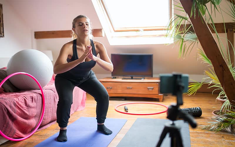 A woman doing squats at home during an online personal training session.